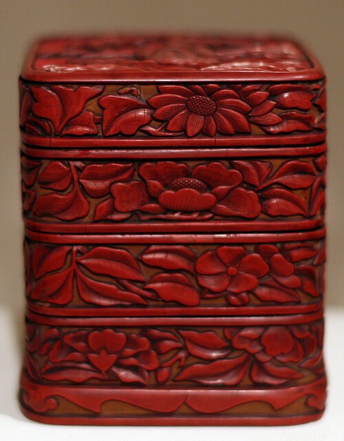 A square tiered red carved lacquer box from the Ming dynasty featuring intricate floral patterns of peonies and chrysanthemums in deep relief