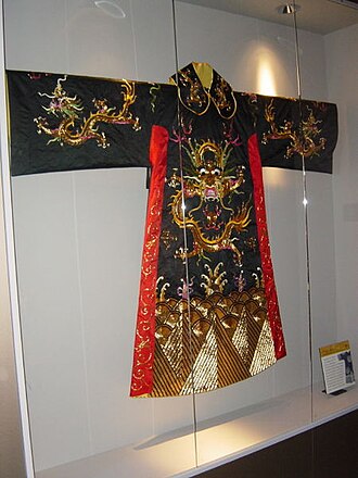 An ornate Qing dynasty dragon robe in black silk with red and gold embroidery of dragons and imperial symbols