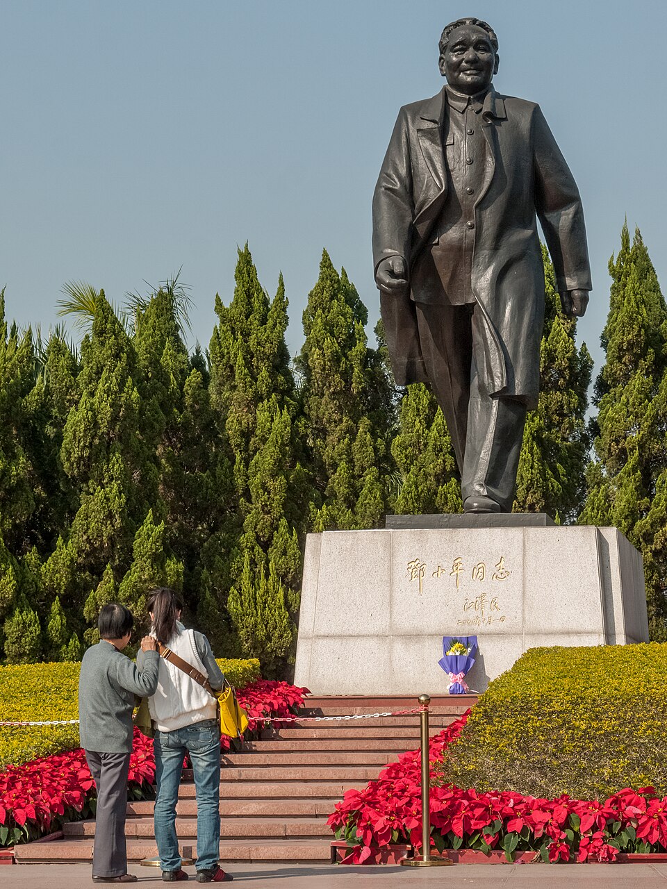 Bronze statue of Deng Xiaoping on a stone pedestal surrounded by red flowers in Shenzhen's Lianhuashan Park