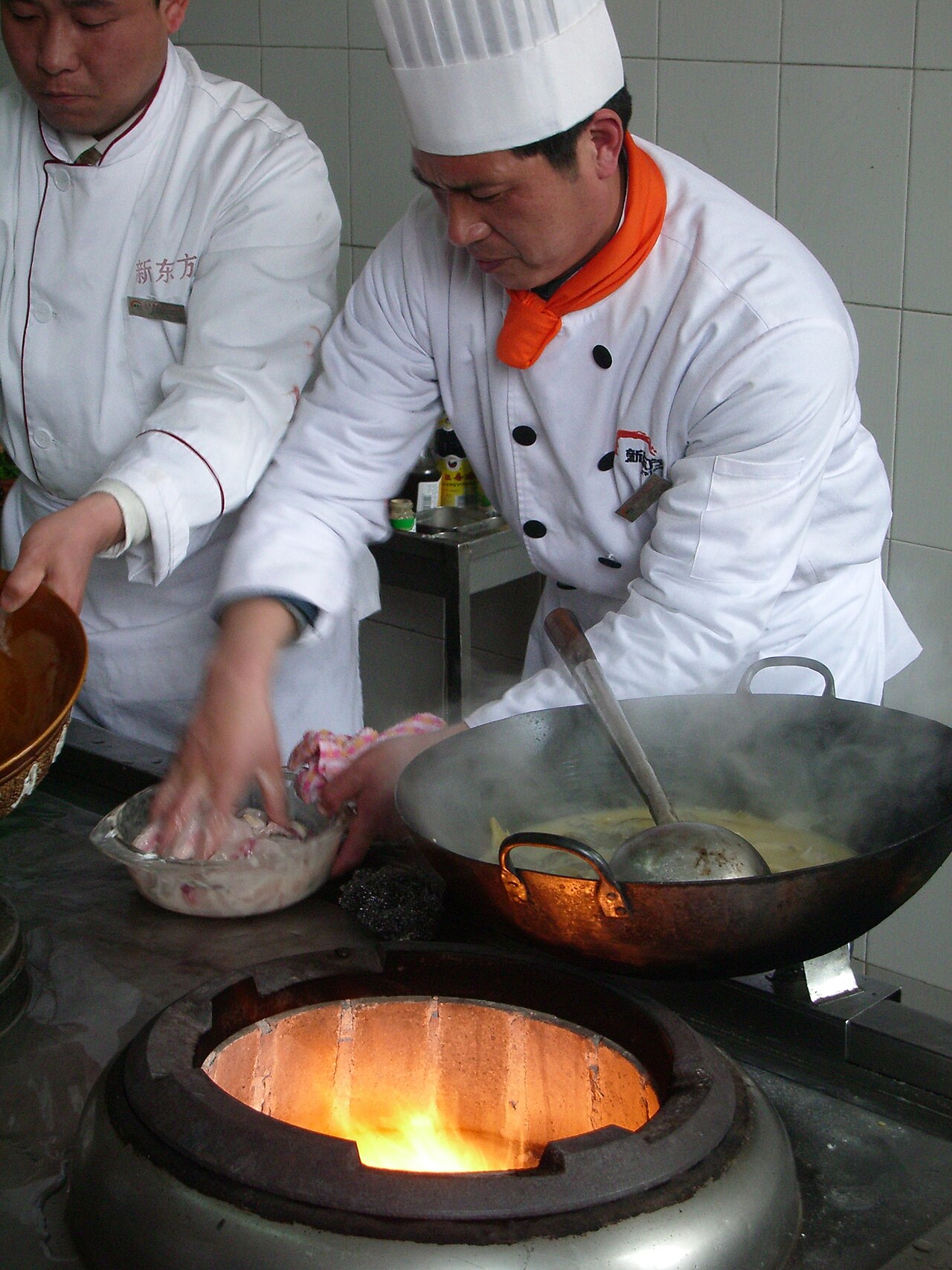 Chinese chefs cooking with woks over high-powered burners in a professional kitchen