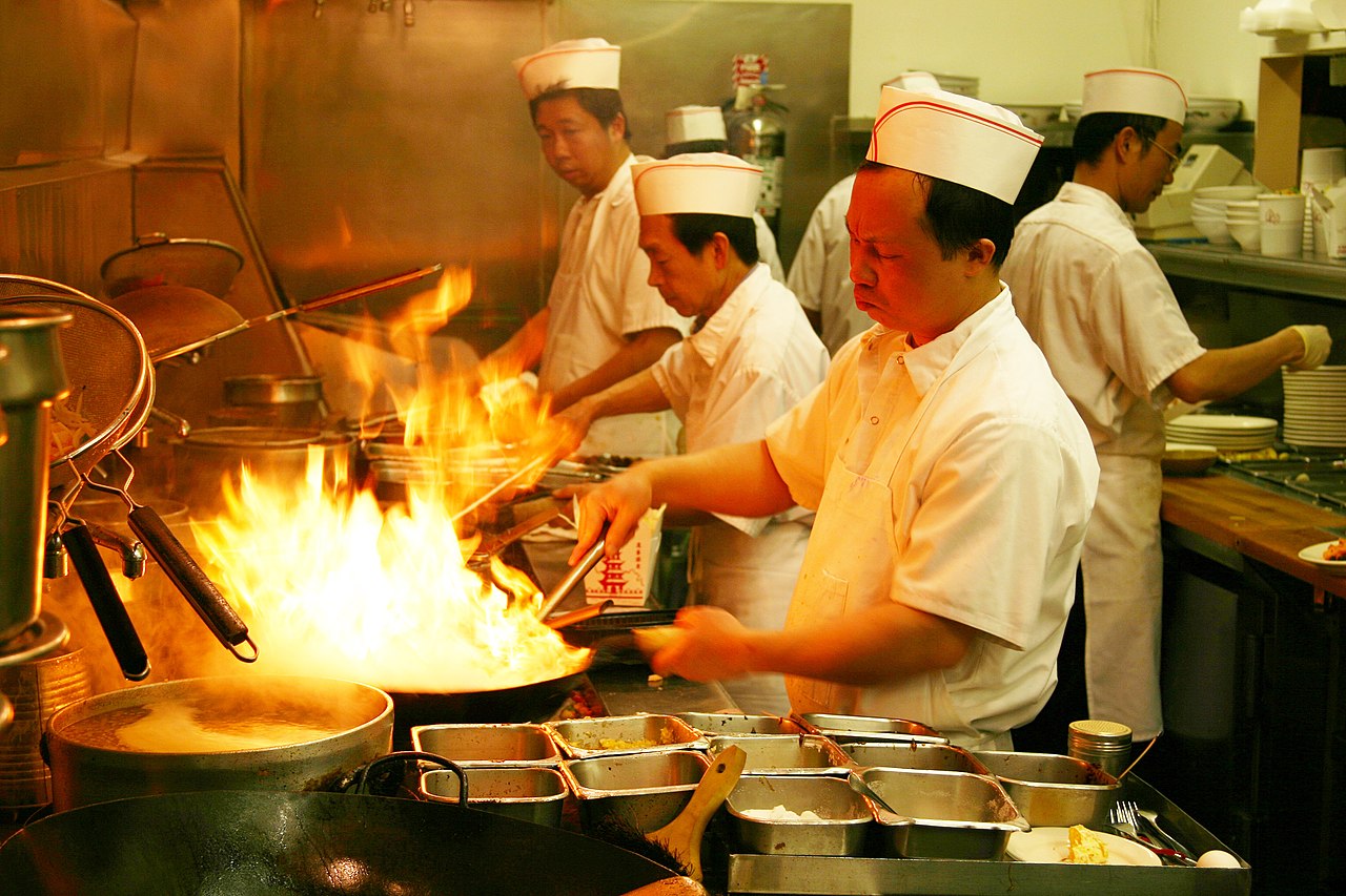 Chinese chef stir-frying with dramatic flames rising from a wok