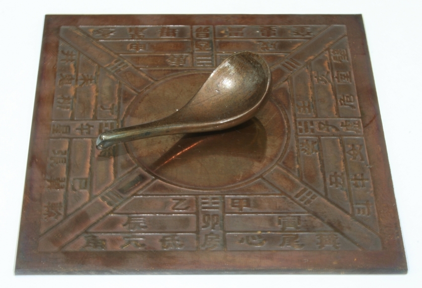 Han dynasty sinan south-pointing spoon compass replica on a bronze plate with Chinese directional markings