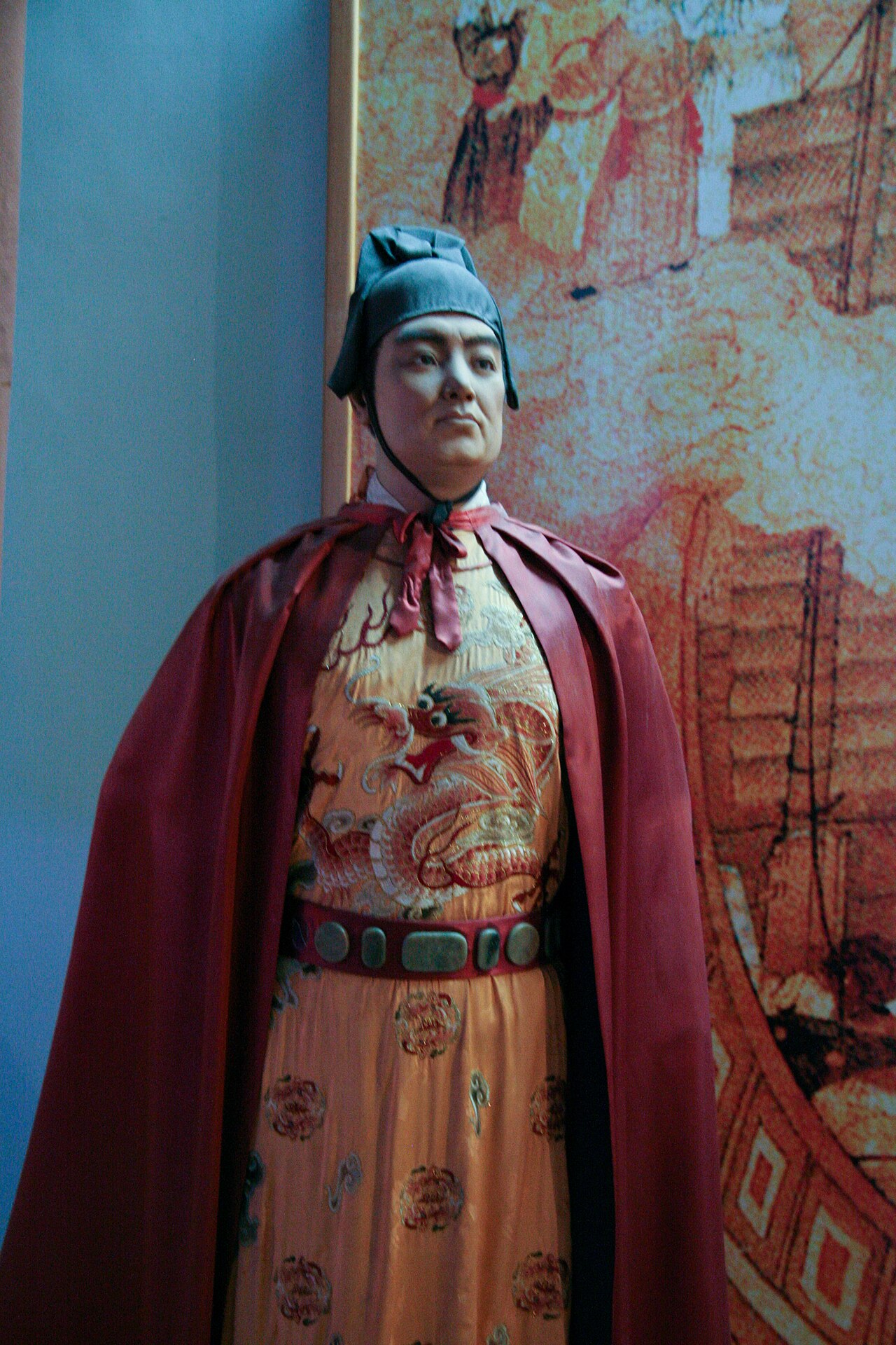 Museum wax figure of Zheng He in Ming dynasty court attire with ships painted in the background
