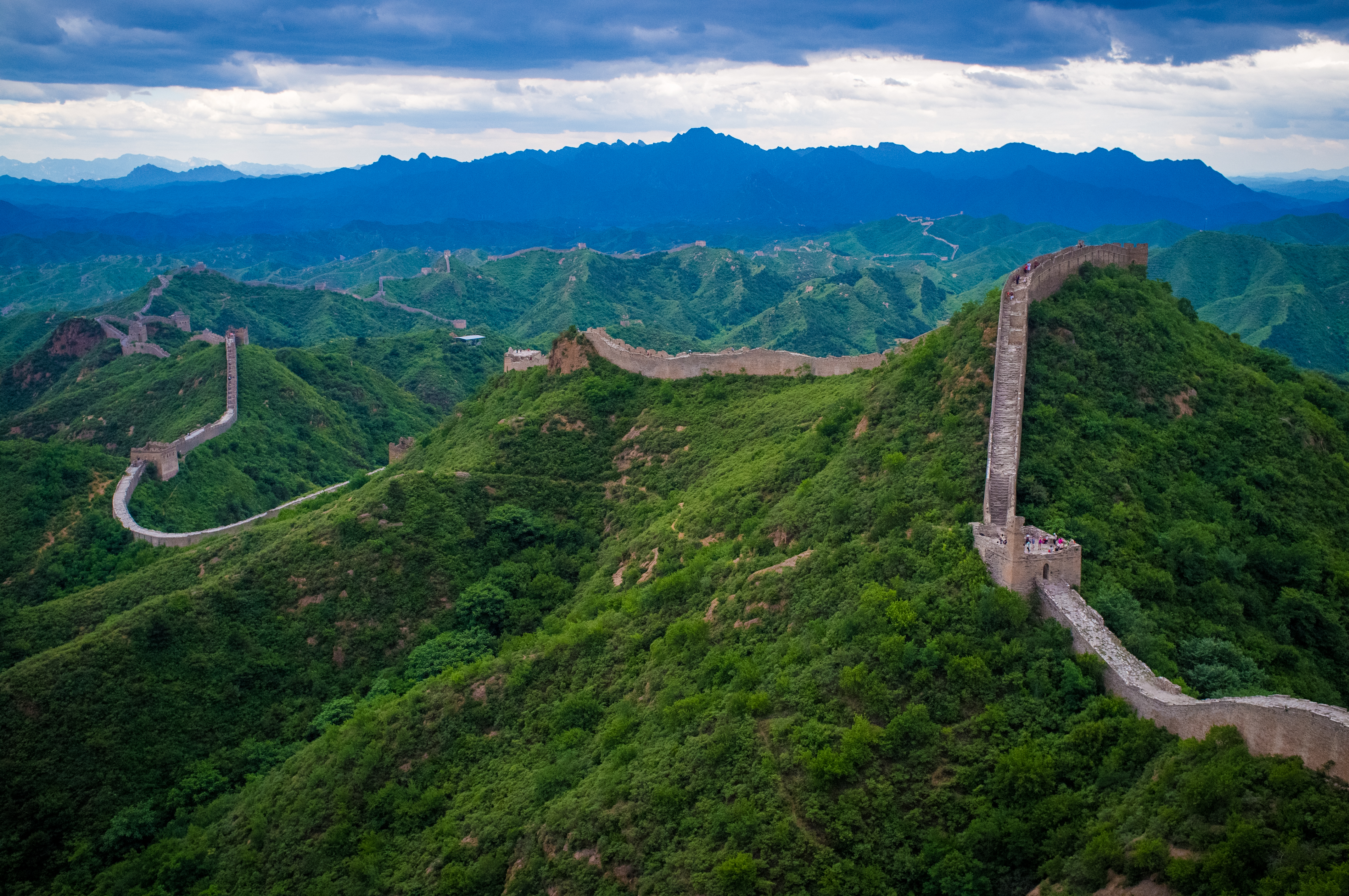 The Great Wall of China stretching across verdant mountainous terrain under dramatic clouds
