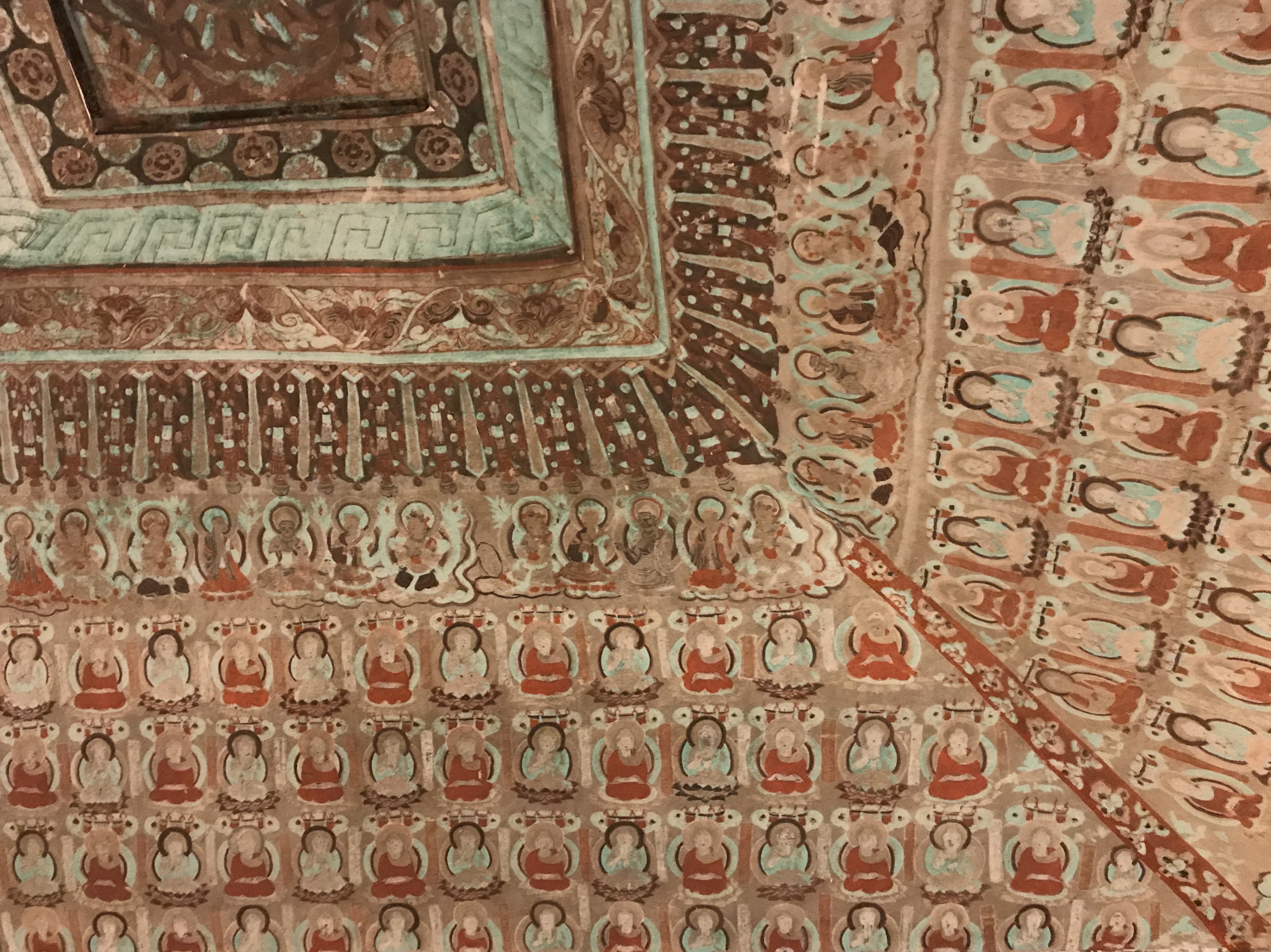 Ornate painted ceiling of a Mogao cave temple at Dunhuang with rows of seated Buddha figures and decorative borders