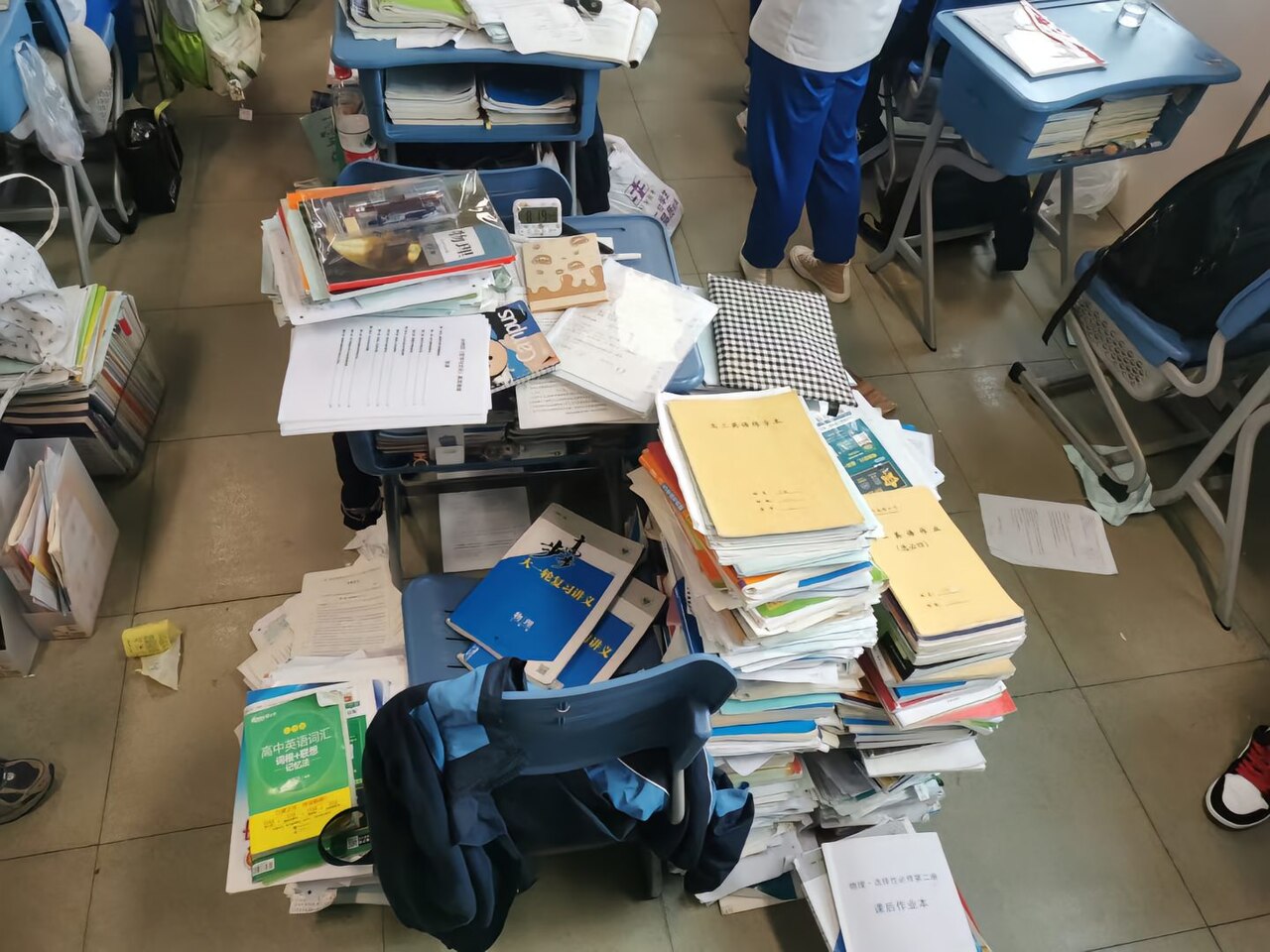 A Chinese high school student's desk overflowing with stacked textbooks and study materials for gaokao preparation