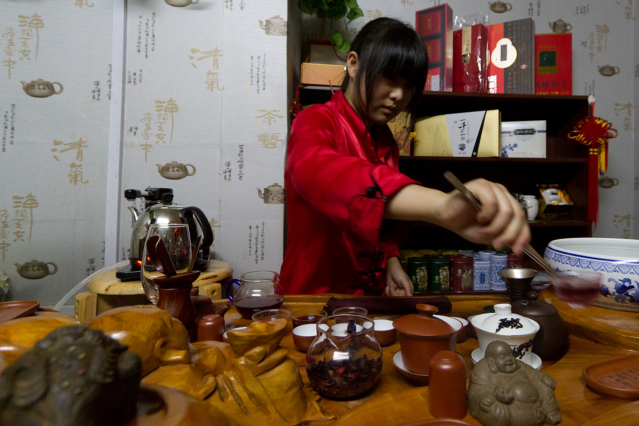 Woman in red performing a gongfu tea ceremony in Shanghai with traditional tea set, Yixing teapots, and calligraphy-decorated walls