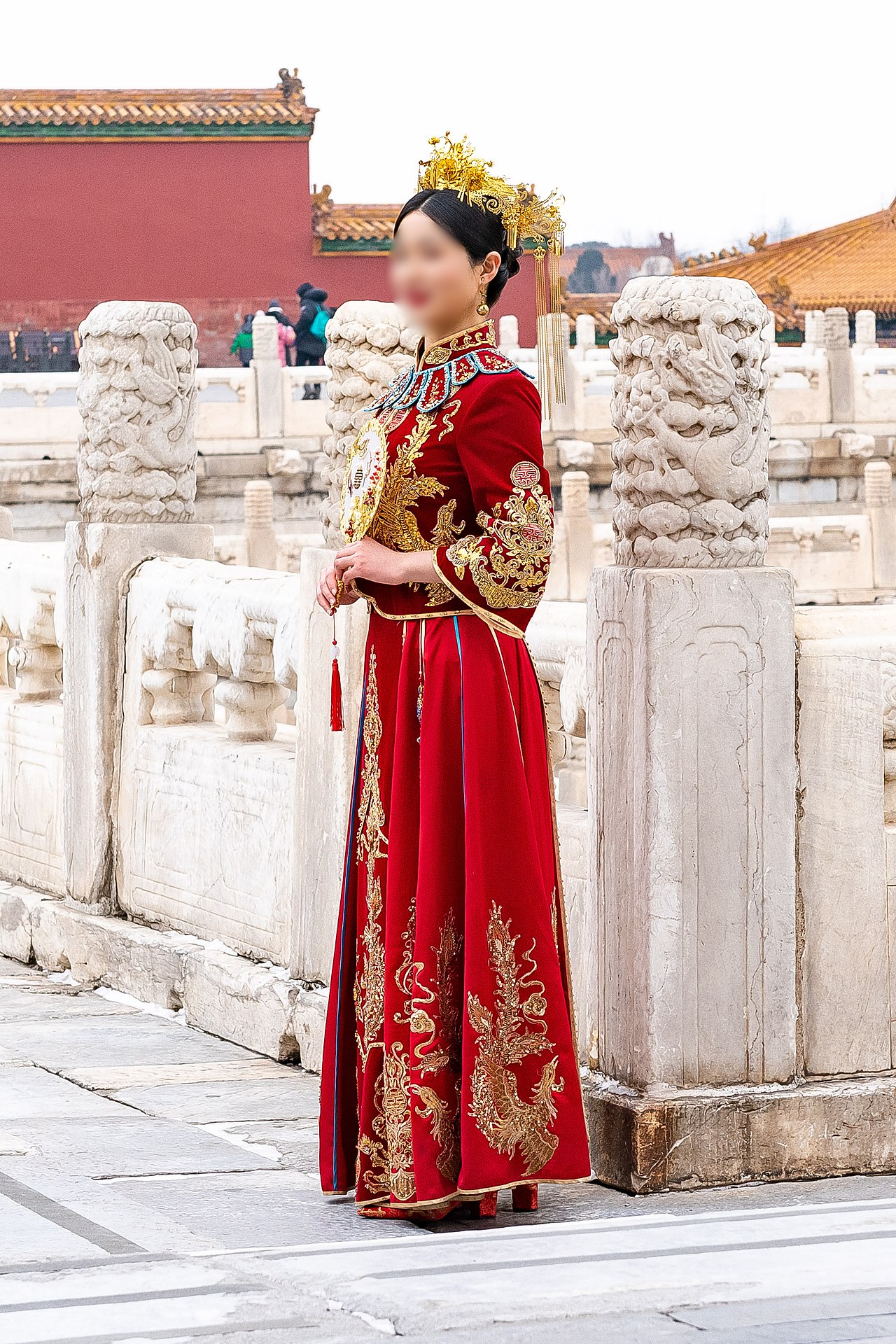 Chinese bride wearing an ornate red xiuhe wedding dress with gold embroidery and traditional headdress posing at the Forbidden City in Beijing