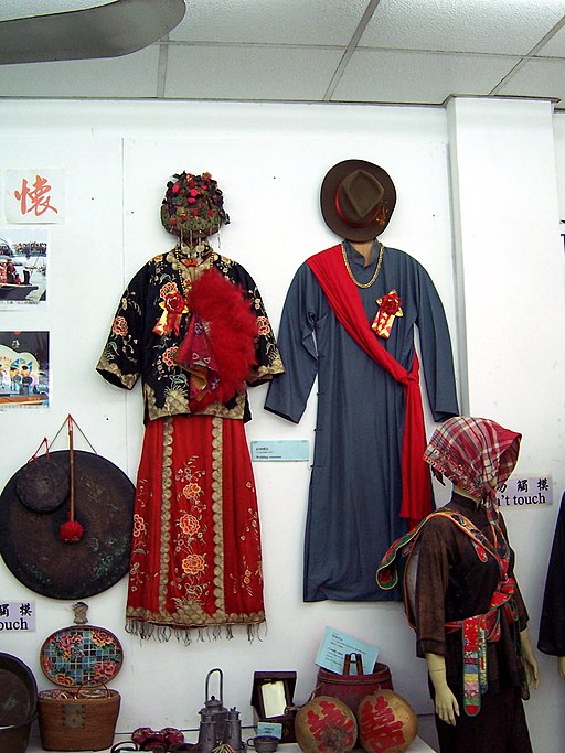Traditional Chinese wedding dresses on display: an embroidered red bridal outfit with headdress and a blue groom's robe with red sash