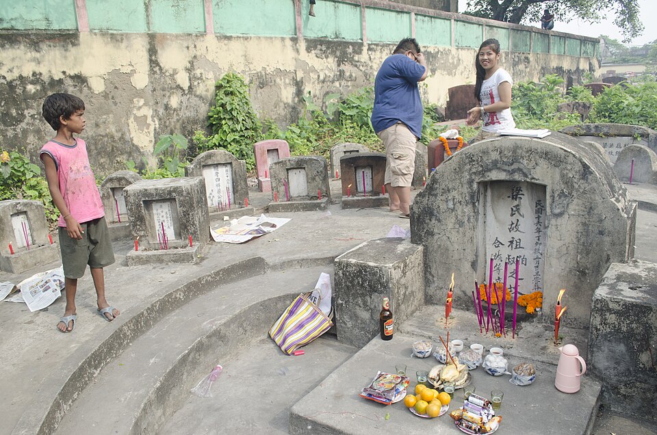 Hillside Chinese cemetery with families tending graves, burning incense and spirit money among the tombstones