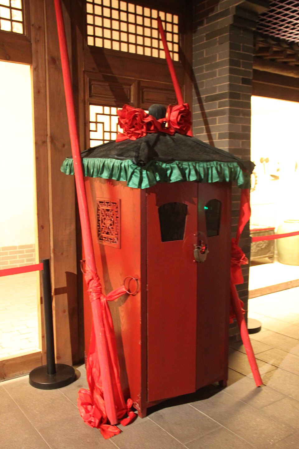Traditional Chinese red bridal sedan chair on display with black canopy and decorative trim