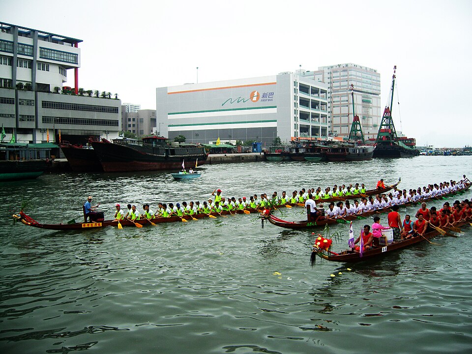 Dragon boat crews racing in a harbor during Dragon Boat Festival with paddlers in synchronized strokes