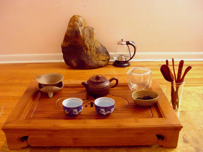 Gongfu tea ceremony setup with Yixing teapot, blue-and-white cups, and tea tools on a bamboo tray